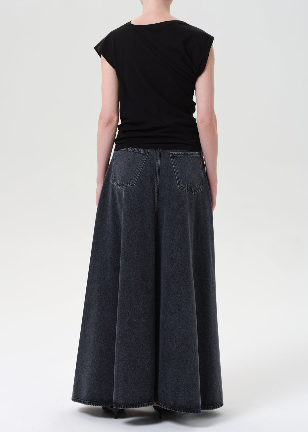 Person wearing a black top and long dark denim skirt on a white background