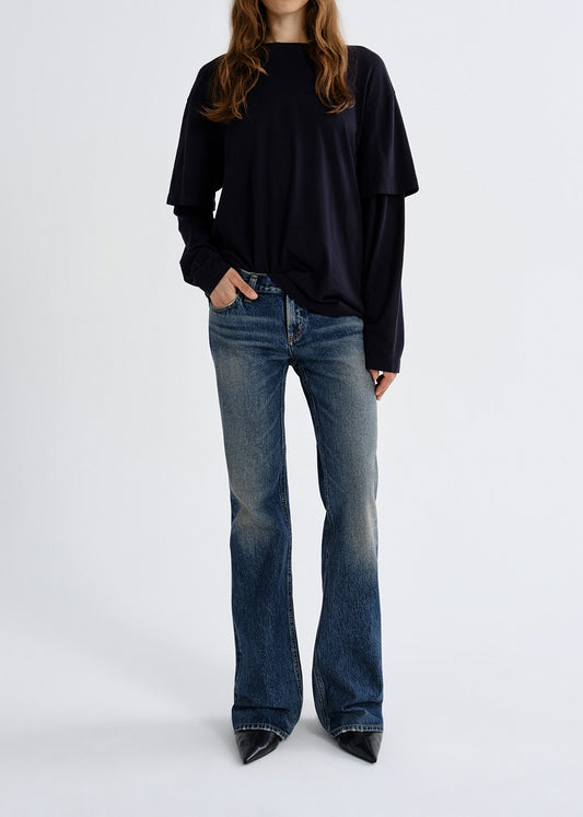 Person wearing a black oversized shirt and blue jeans on a grey background