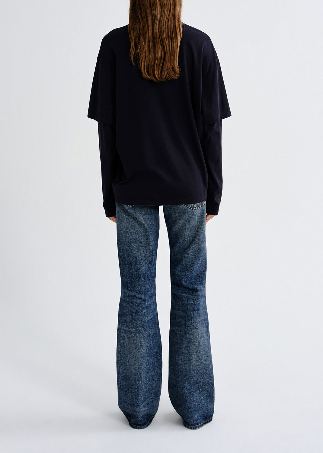 Person wearing a black oversized shirt and blue jeans on a grey background