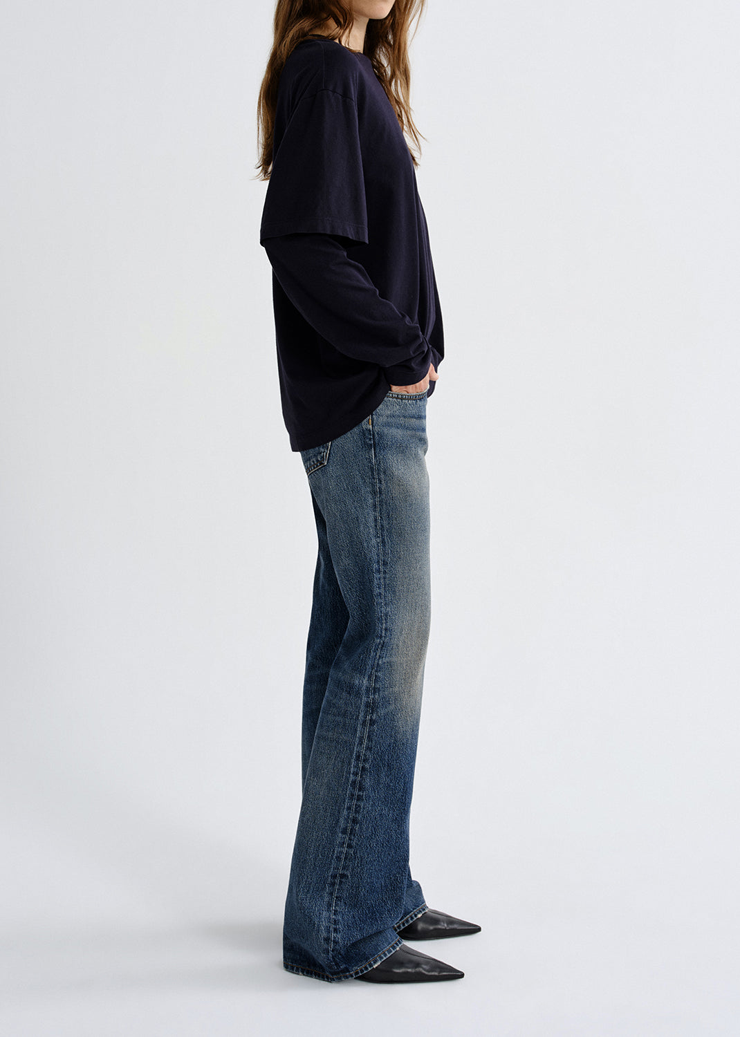 Person wearing a black oversized sweatshirt and blue jeans on a grey background