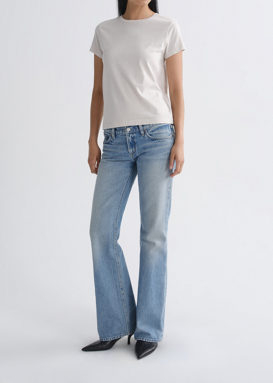 Person wearing light blue flared jeans and a white t-shirt on a grey background