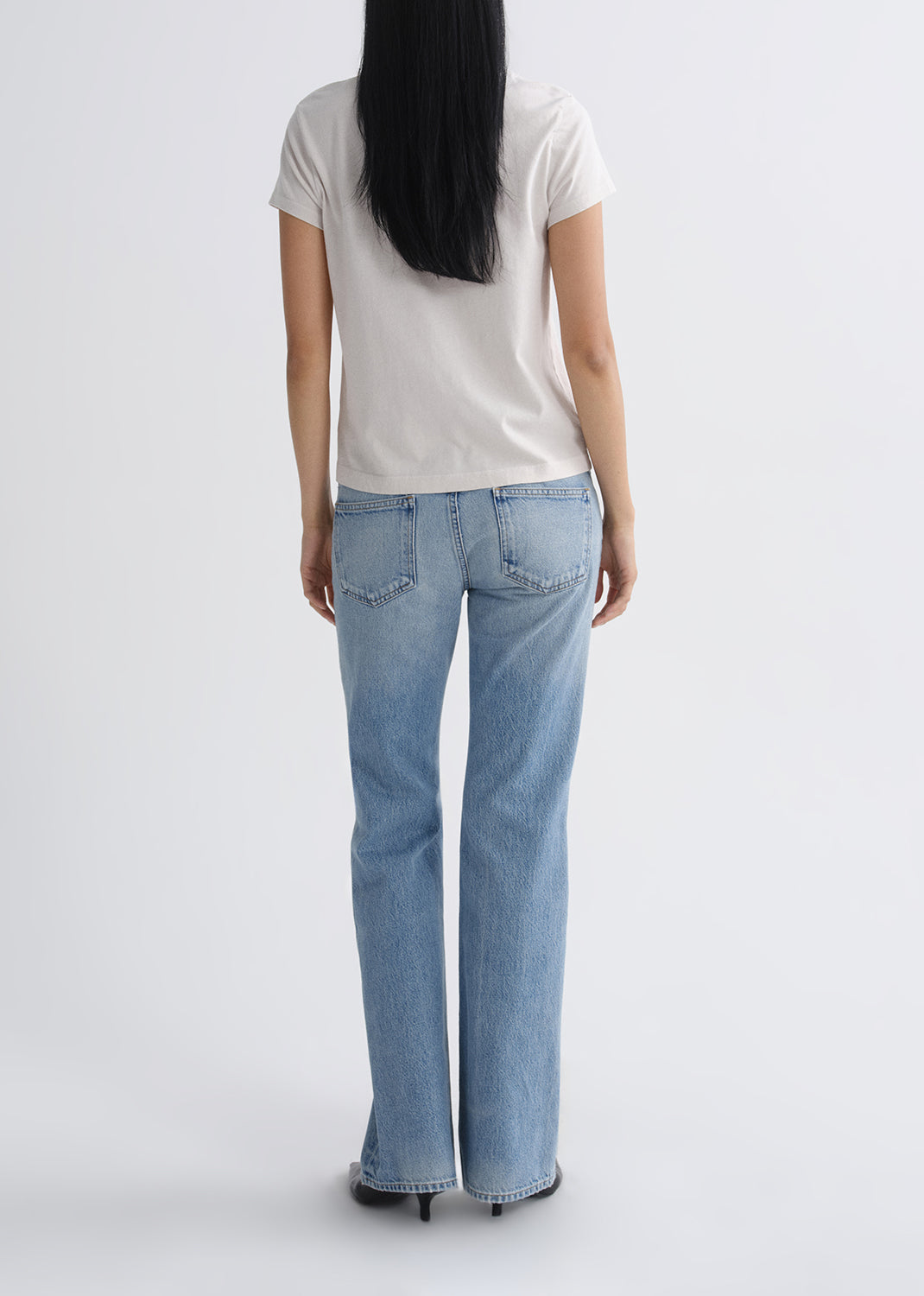 Person wearing light blue jeans and a white t-shirt on a grey background