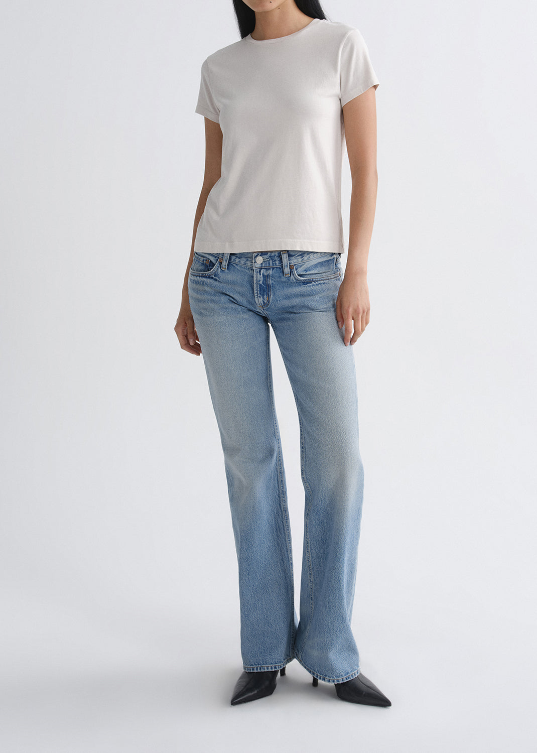 Person wearing a white t-shirt and light blue jeans on a grey background