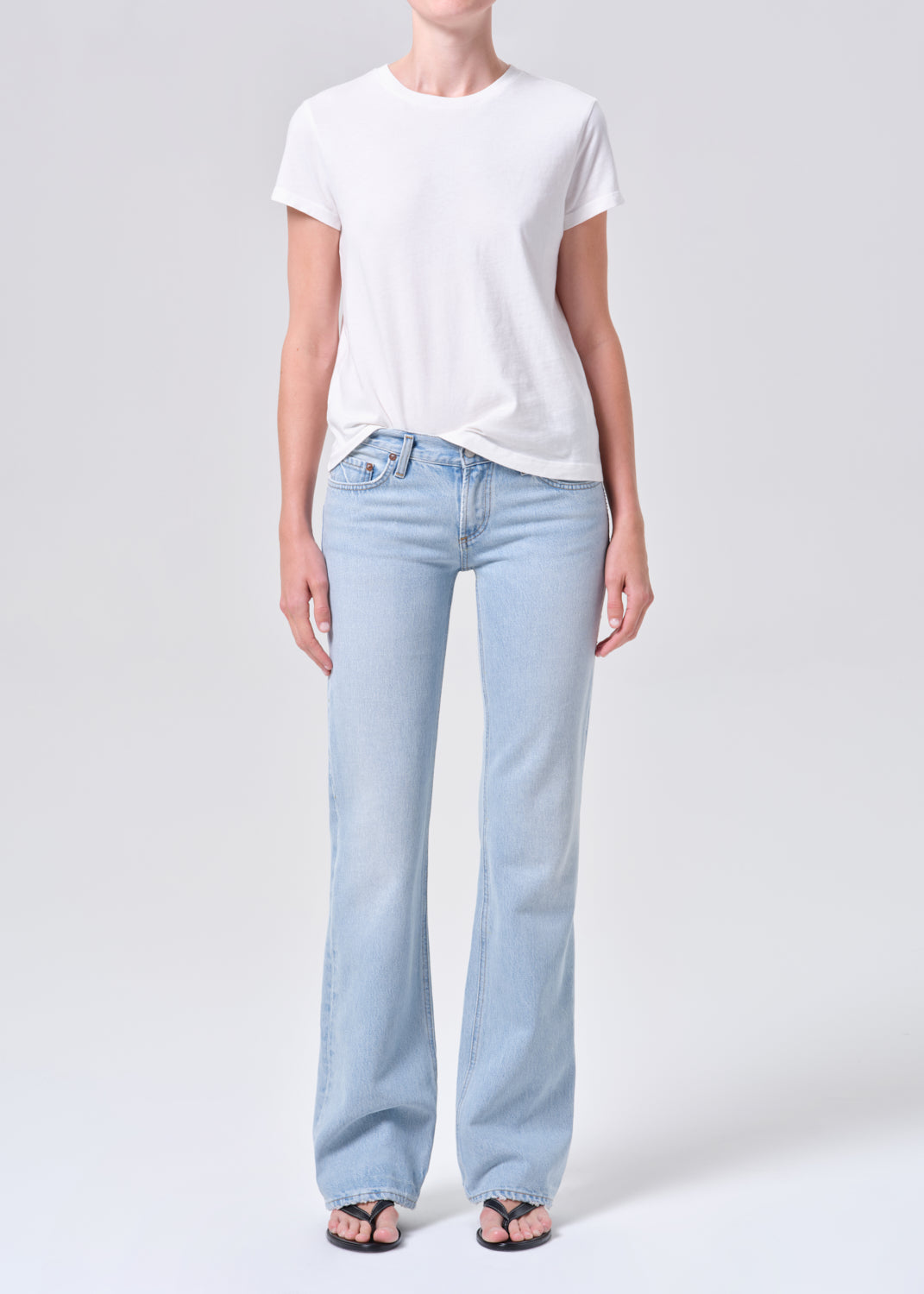 Person wearing light blue jeans and a white t-shirt on a plain background