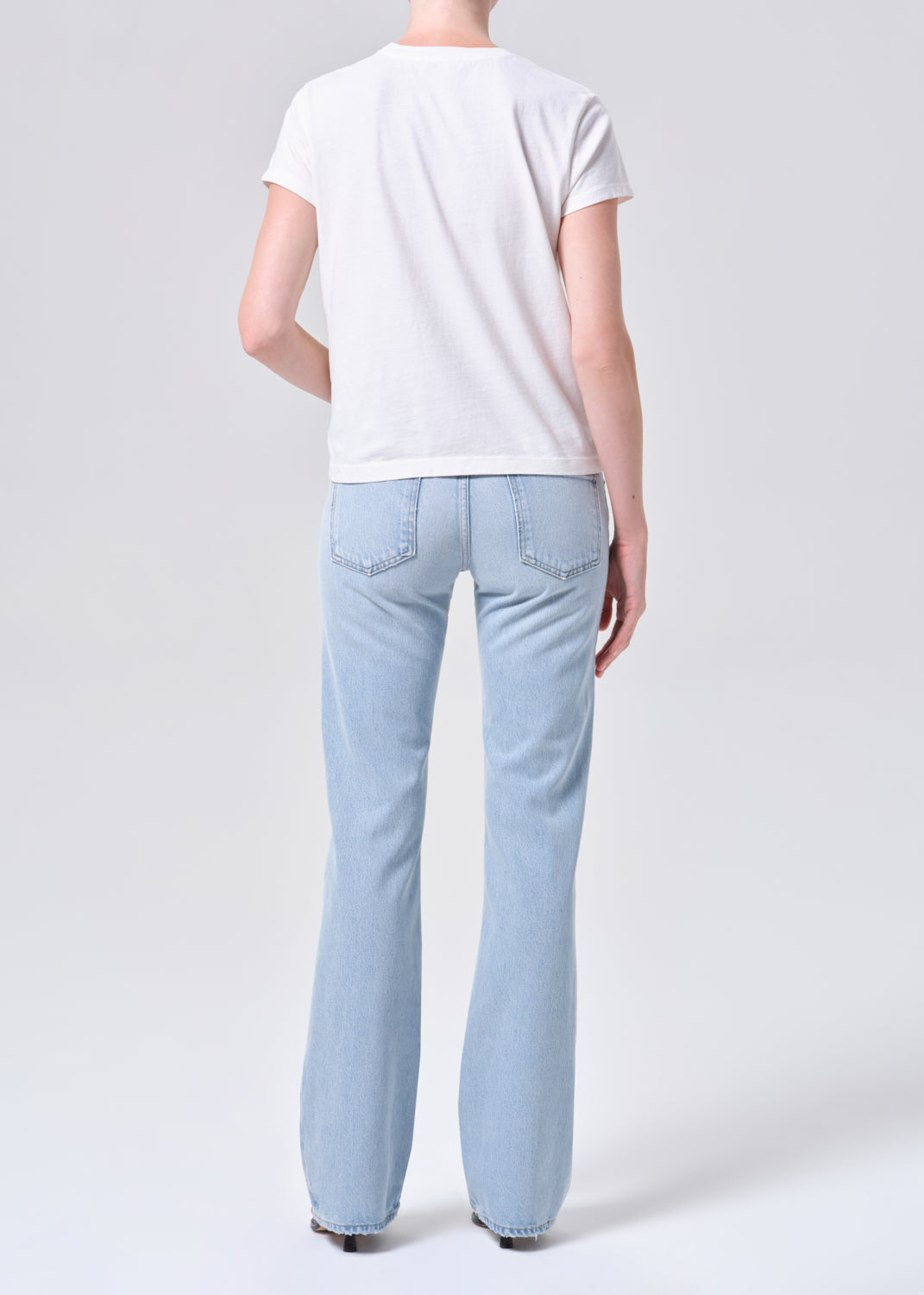 Person wearing light blue jeans and a white t-shirt on a plain background