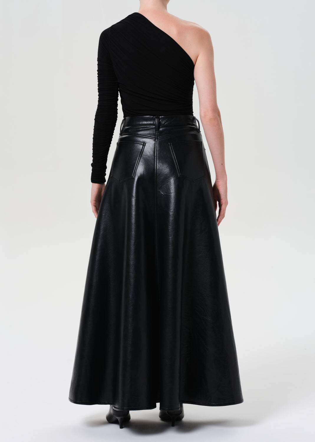 Person wearing a black one-shoulder top and black leather skirt on a white background