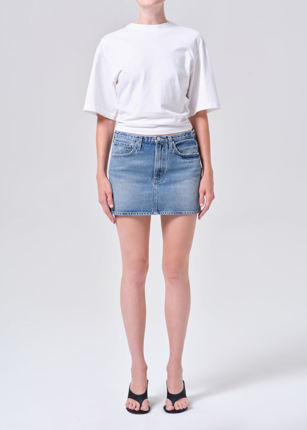 Person wearing a white t-shirt and denim skirt on a plain background