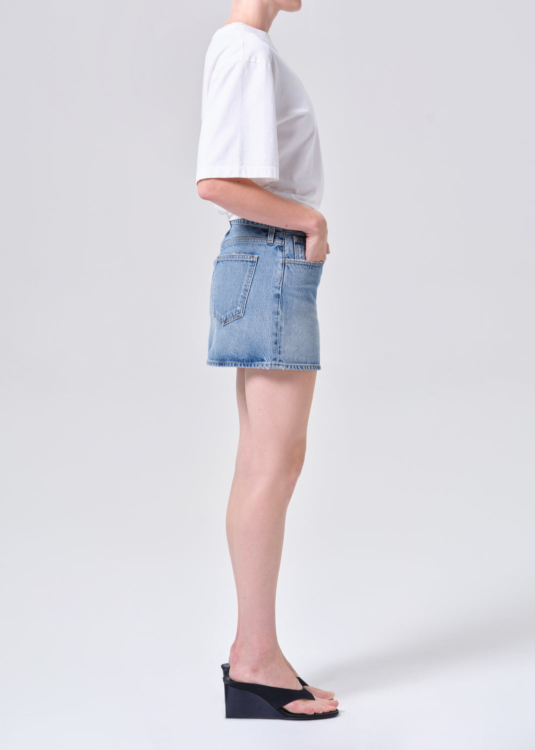 Person wearing a white t-shirt and denim skirt on a plain background