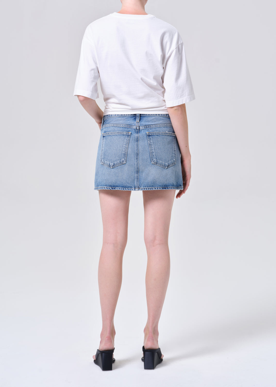 Person wearing a white t-shirt and denim skirt on a plain background
