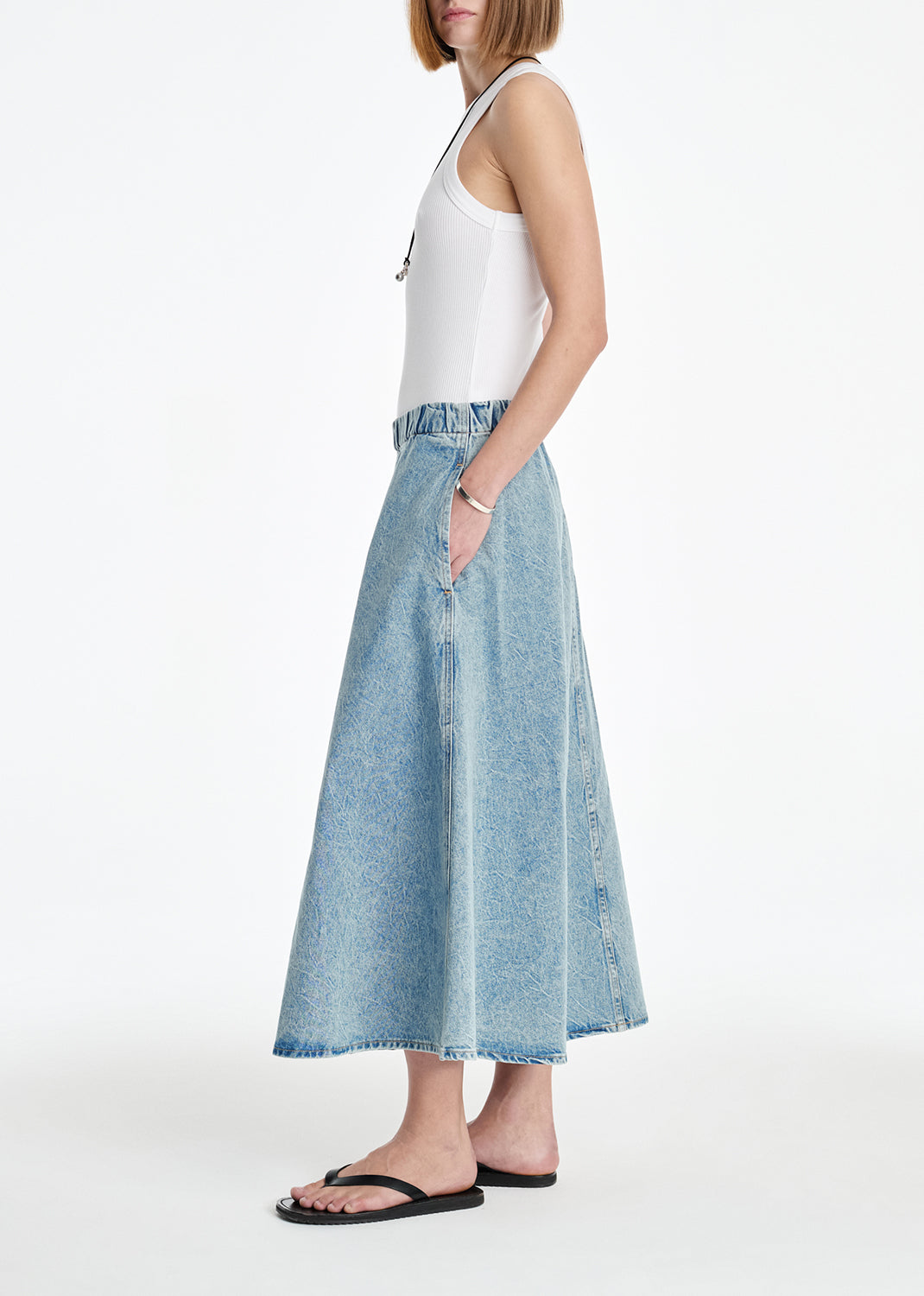 Person wearing a white sleeveless top and blue denim skirt on a white background