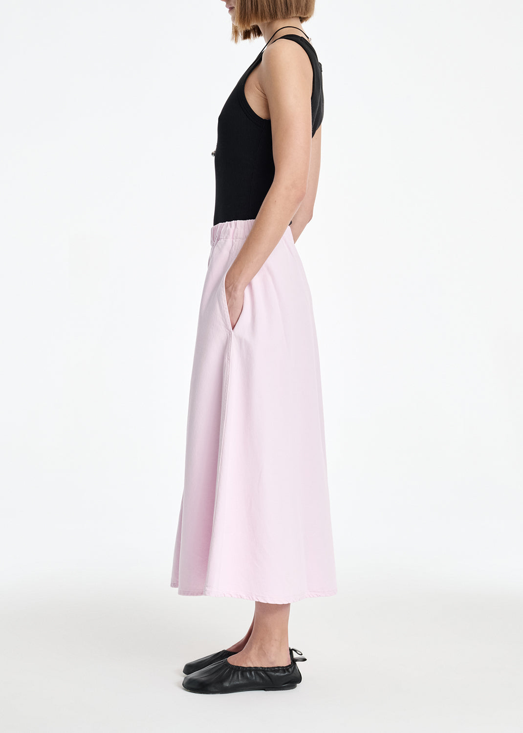 Person wearing a black top and light pink skirt on a white background