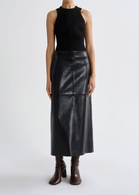 A model wearing a black sleeveless knit top and a black faux-leather midi skirt, paired with dark brown heeled ankle boots, against a grey background.