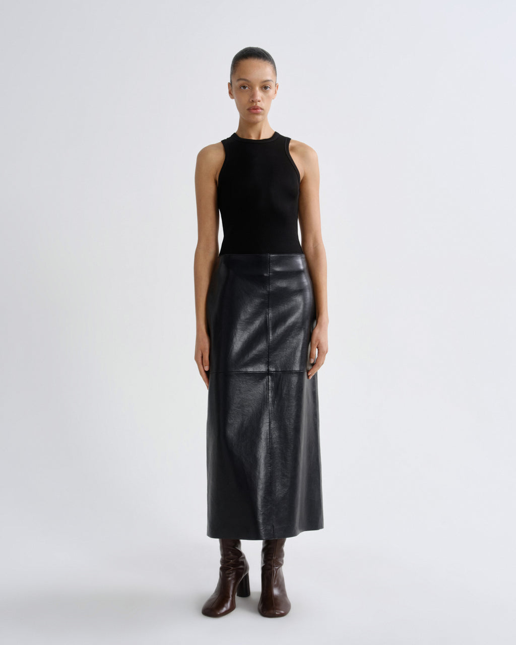 Person wearing a black sleeveless top and leather skirt on a white background
