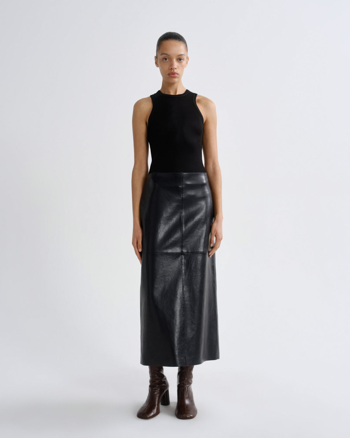 Person wearing a black sleeveless top and leather skirt on a white background