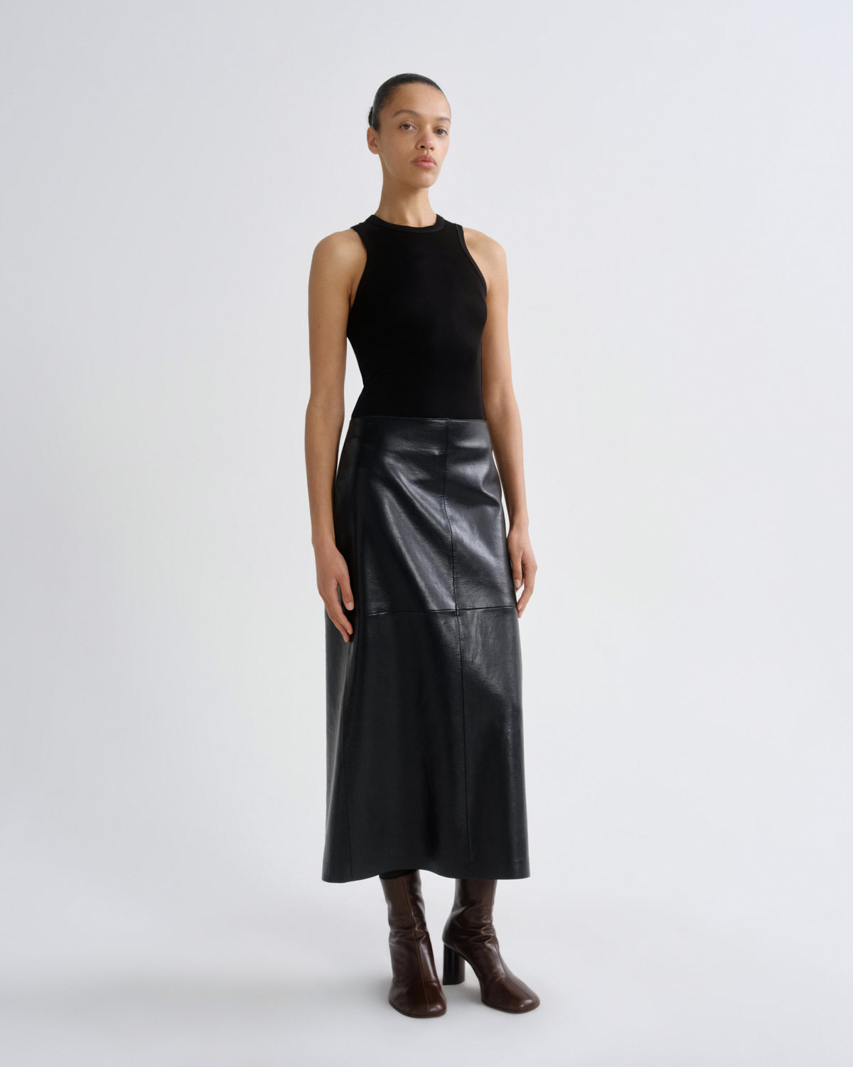 Person wearing a black sleeveless top and leather skirt on a white background