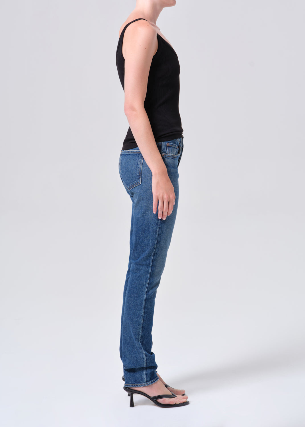 Person wearing blue jeans and a black top on a white background