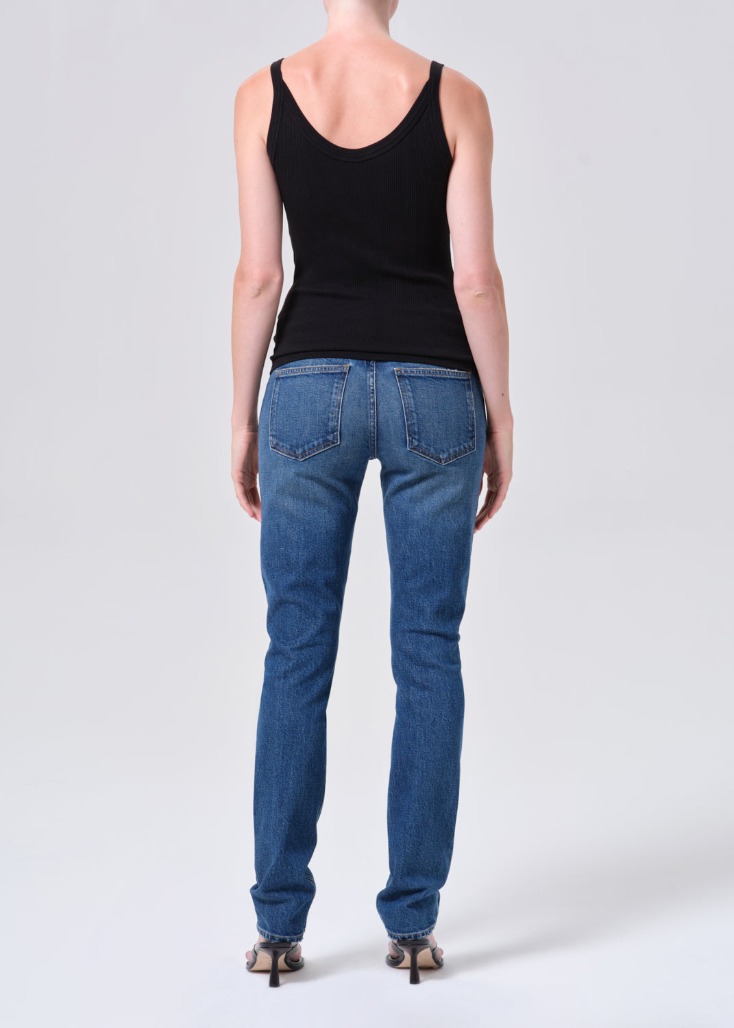 Person wearing blue jeans and a black tank top on a white background