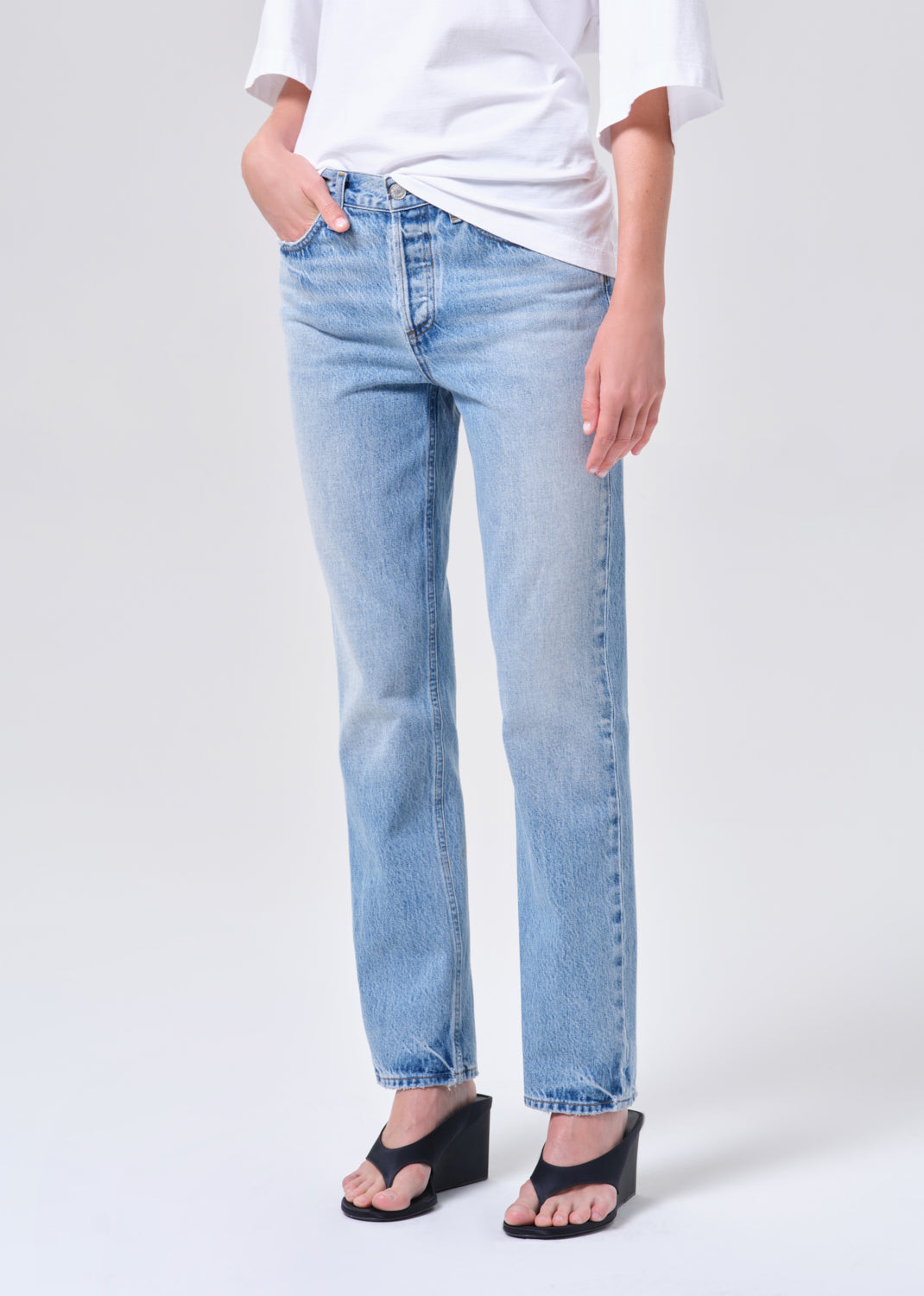 Person wearing light blue jeans and a white shirt on a white background