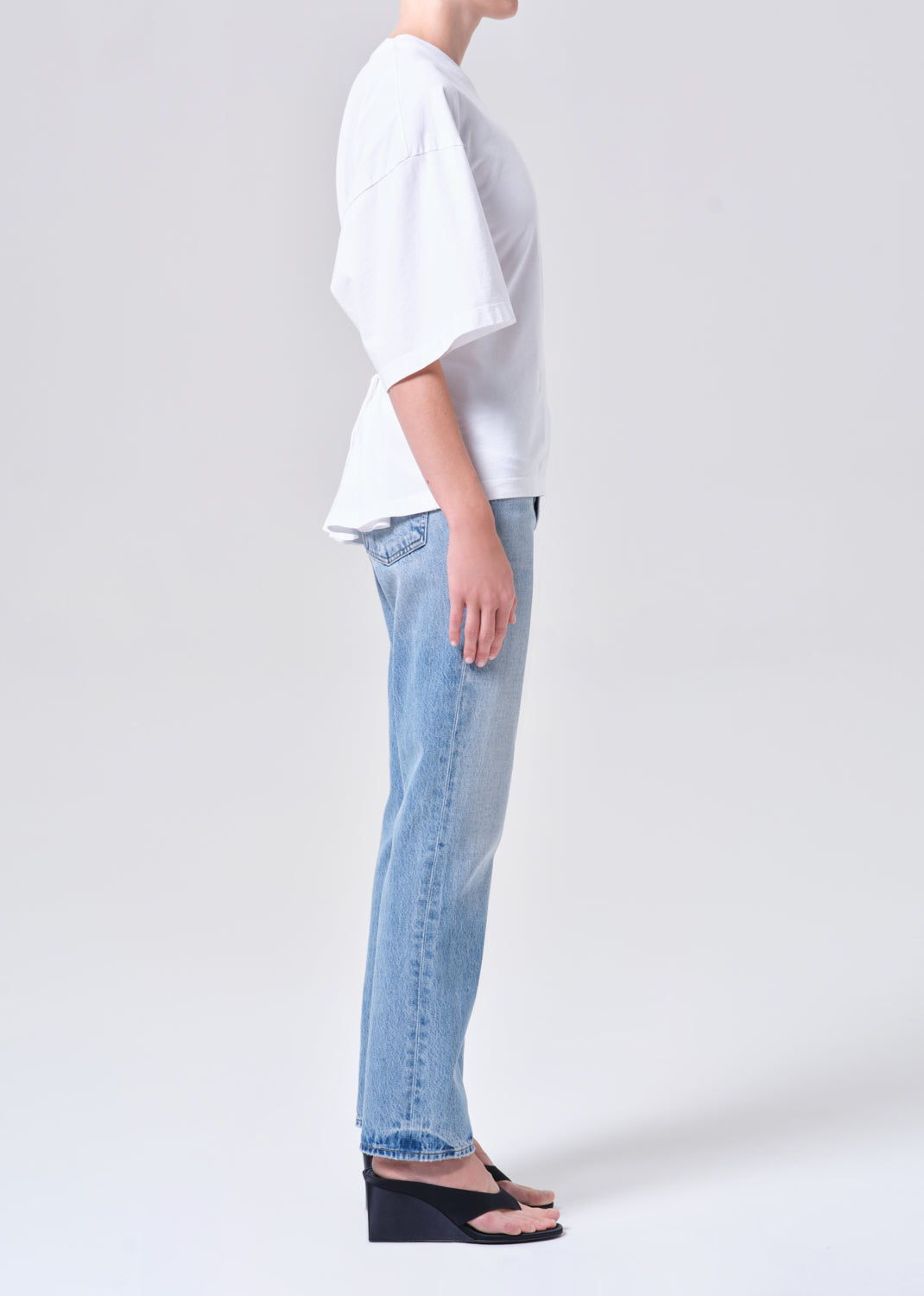 Person wearing a white shirt and light blue jeans on a plain background