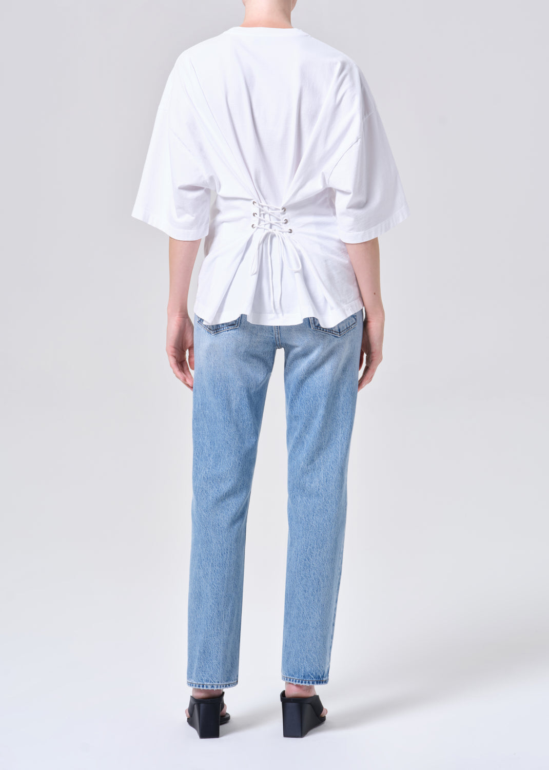 Person wearing a white top with a knot detail and light blue jeans on a plain background