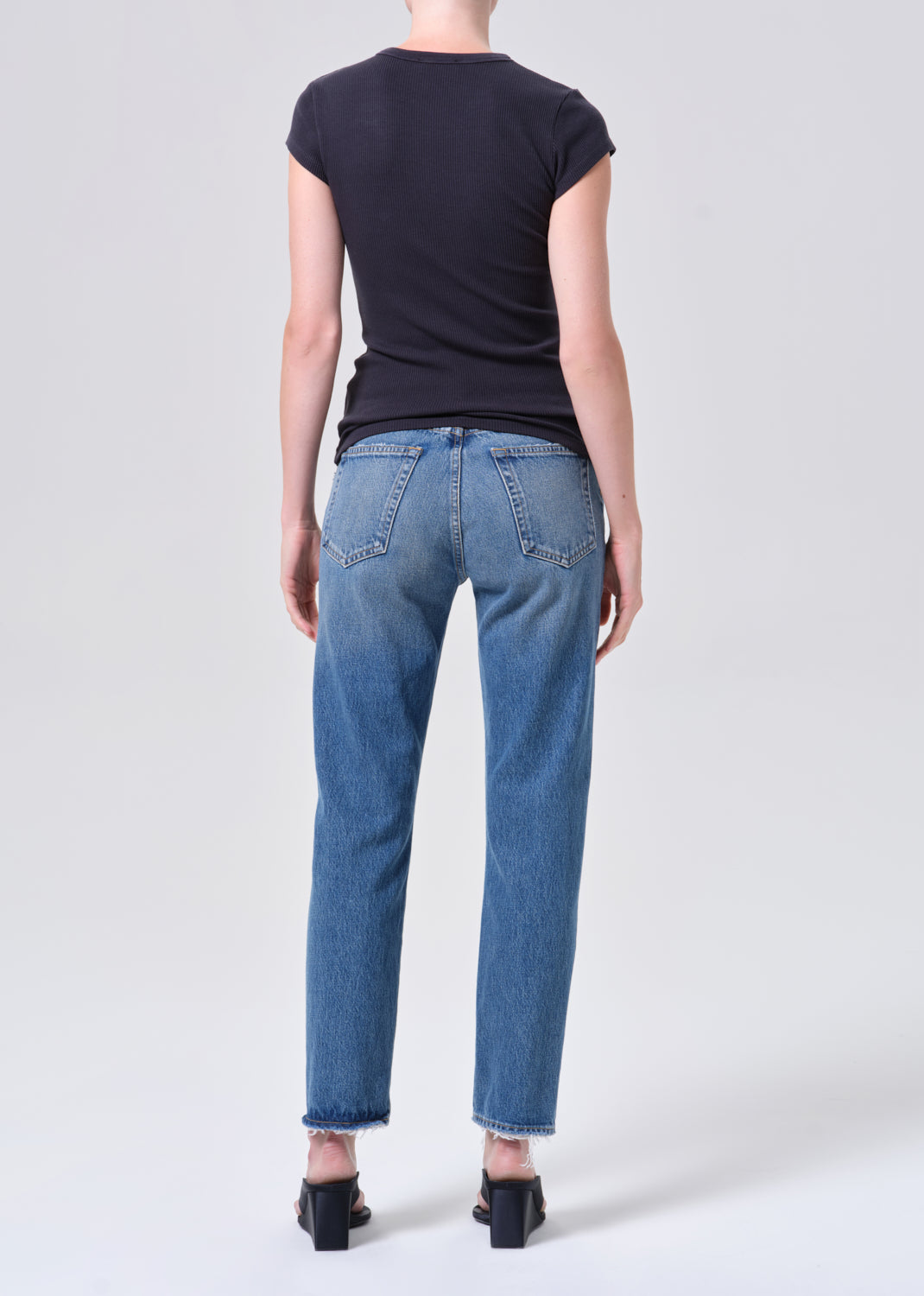 Person wearing blue jeans and a black top on a white background