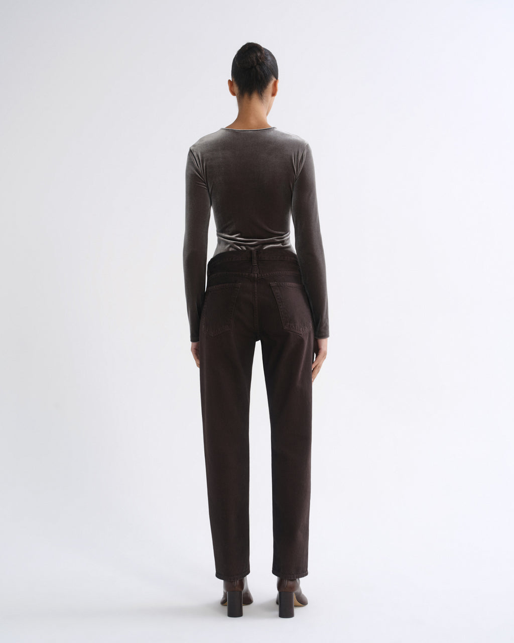 A model viewed from the back wearing a dark brown long-sleeve top and matching dark brown trousers, standing against a plain white studio background.