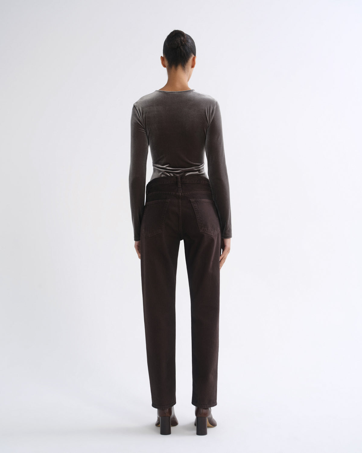 A model viewed from the back wearing a dark brown long-sleeve top and matching dark brown trousers, standing against a plain white studio background.