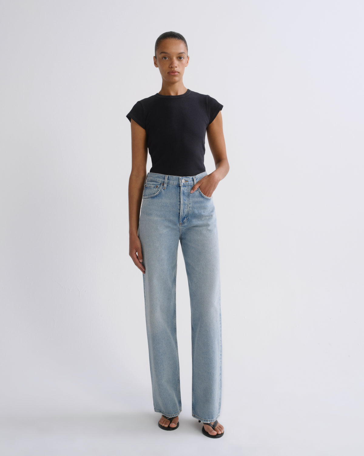 A model stands against a light gray studio background wearing a black short-sleeve crewneck top and light-wash wide-leg jeans.