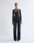 A model stands against a light gray studio background wearing a dark brown long-sleeve velvet top and dark blue wide-leg jeans.