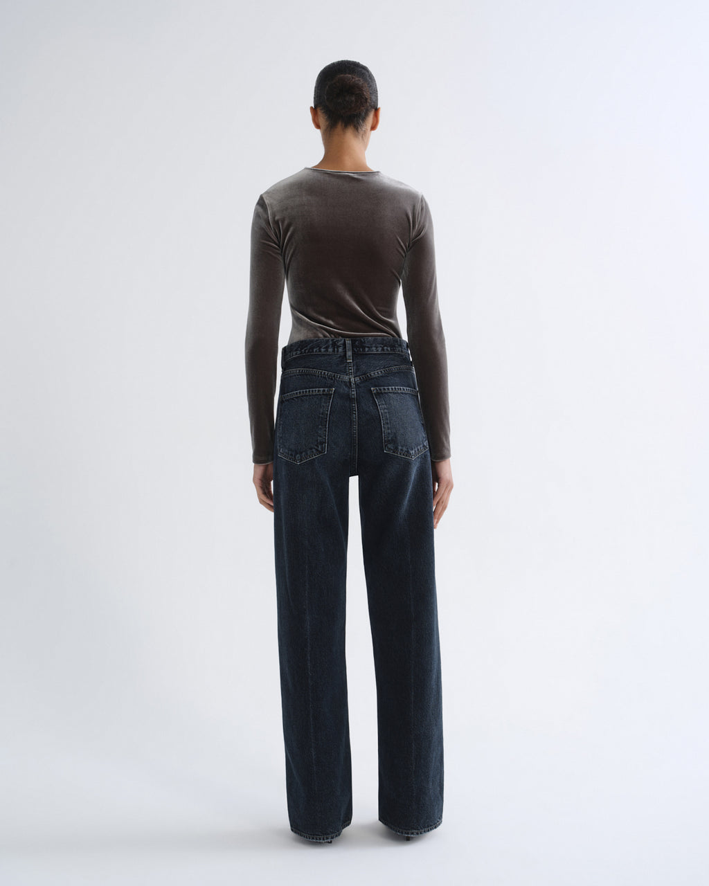 A model shown from the back wearing a dark brown long-sleeve top and dark blue wide-leg jeans against a light gray studio background.