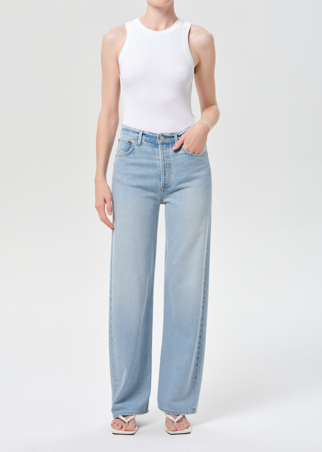 Person wearing a white sleeveless top and light blue jeans on a plain background