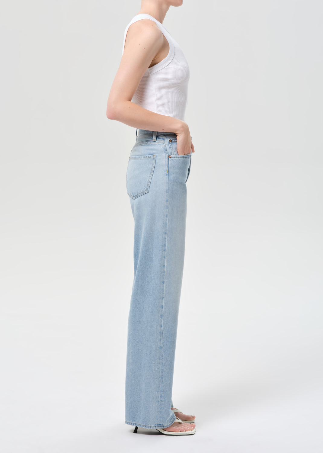 Person wearing light blue jeans and a white top on a plain background