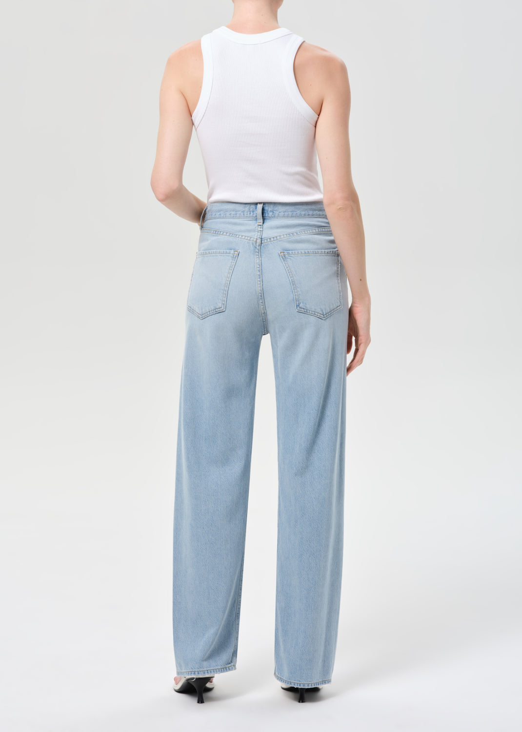 Person wearing light blue jeans and a white sleeveless top on a plain background