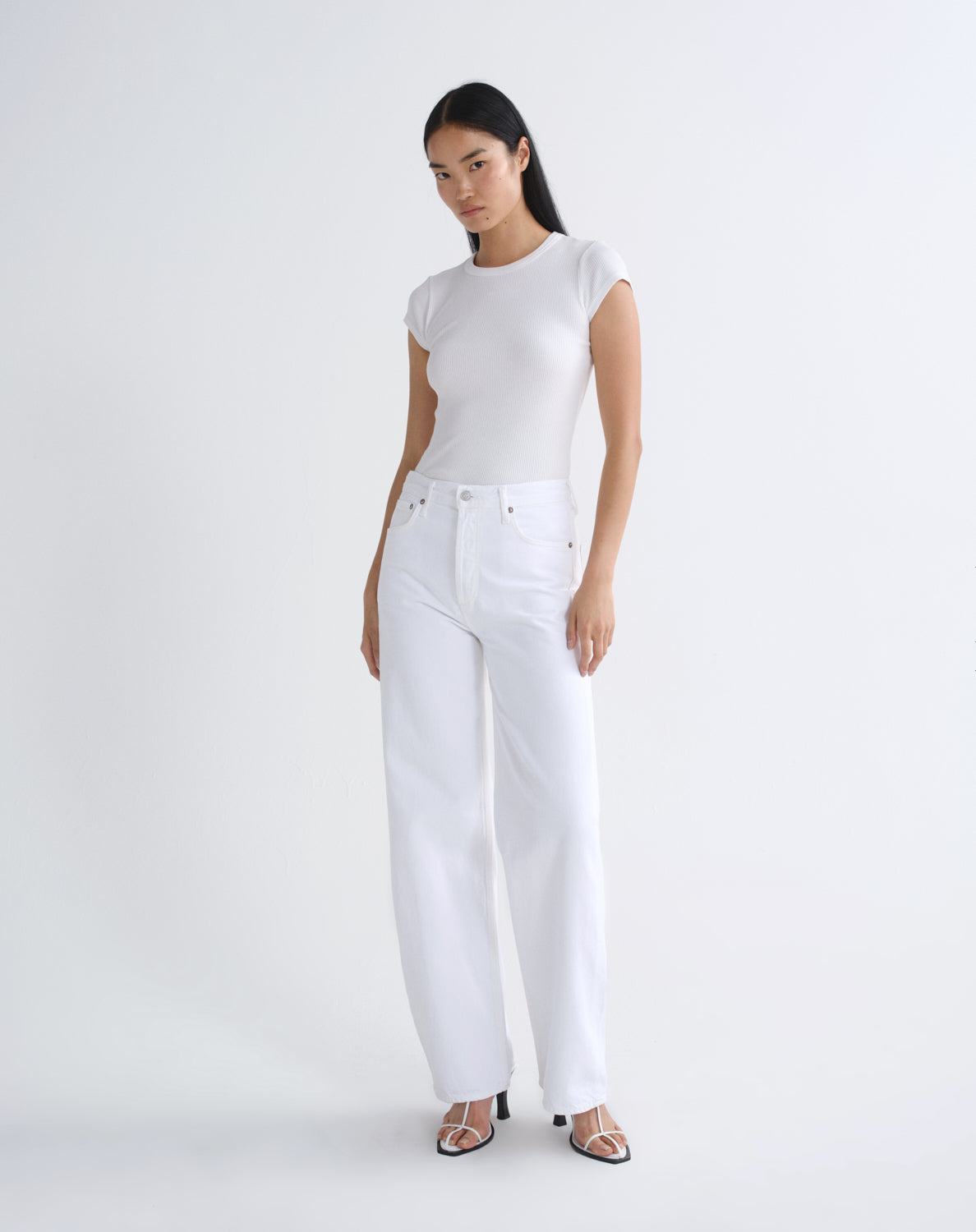 A model wearing a white short-sleeve crewneck top and white wide-leg jeans, standing against a seamless white studio background.
