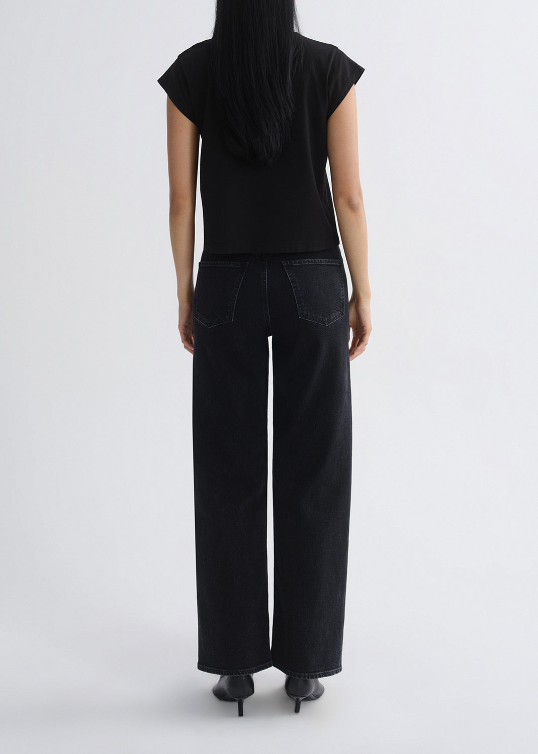 Person wearing a black sleeveless top and wide-leg pants on a grey background
