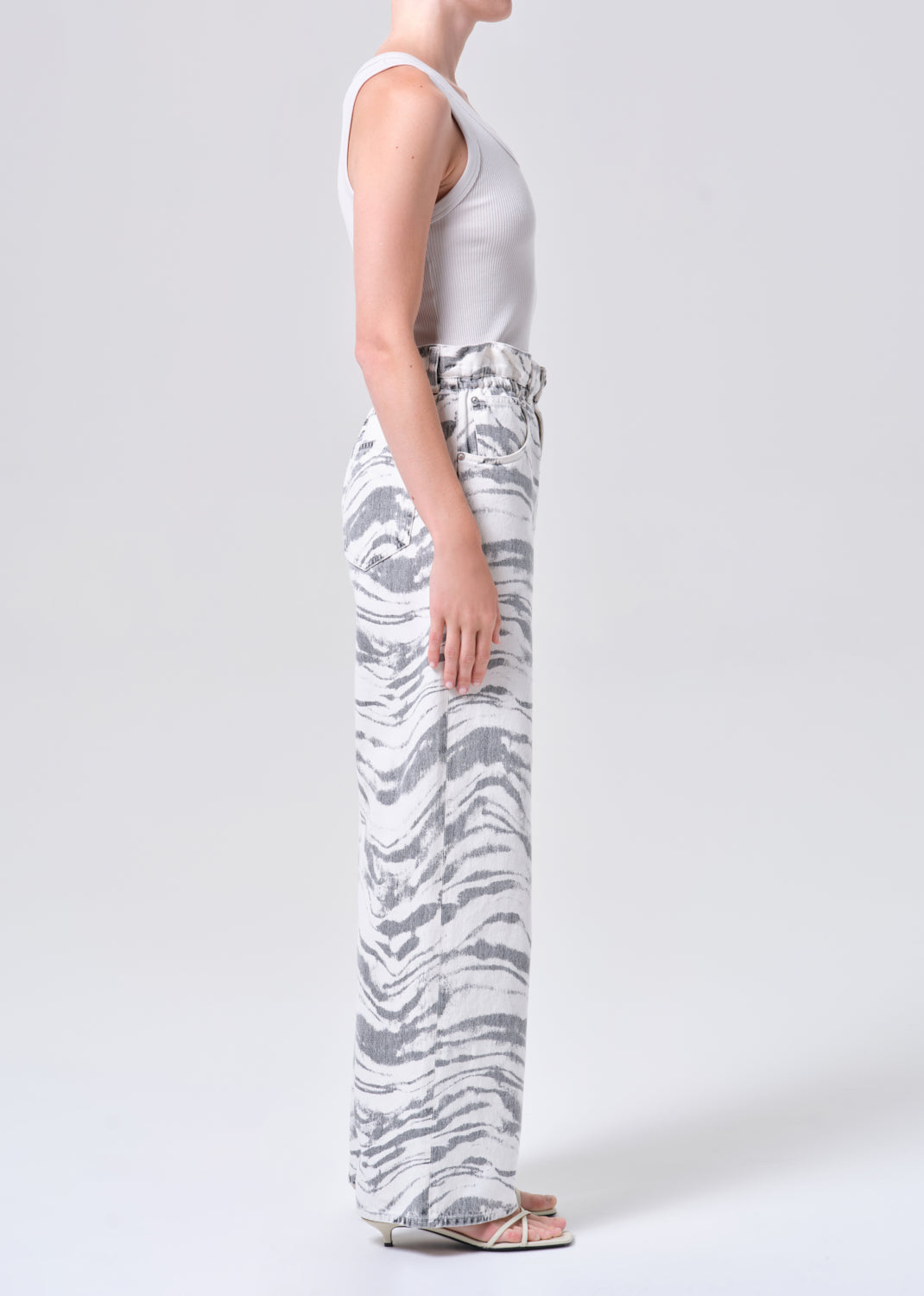 Person wearing a white tank top and patterned pants on a plain background