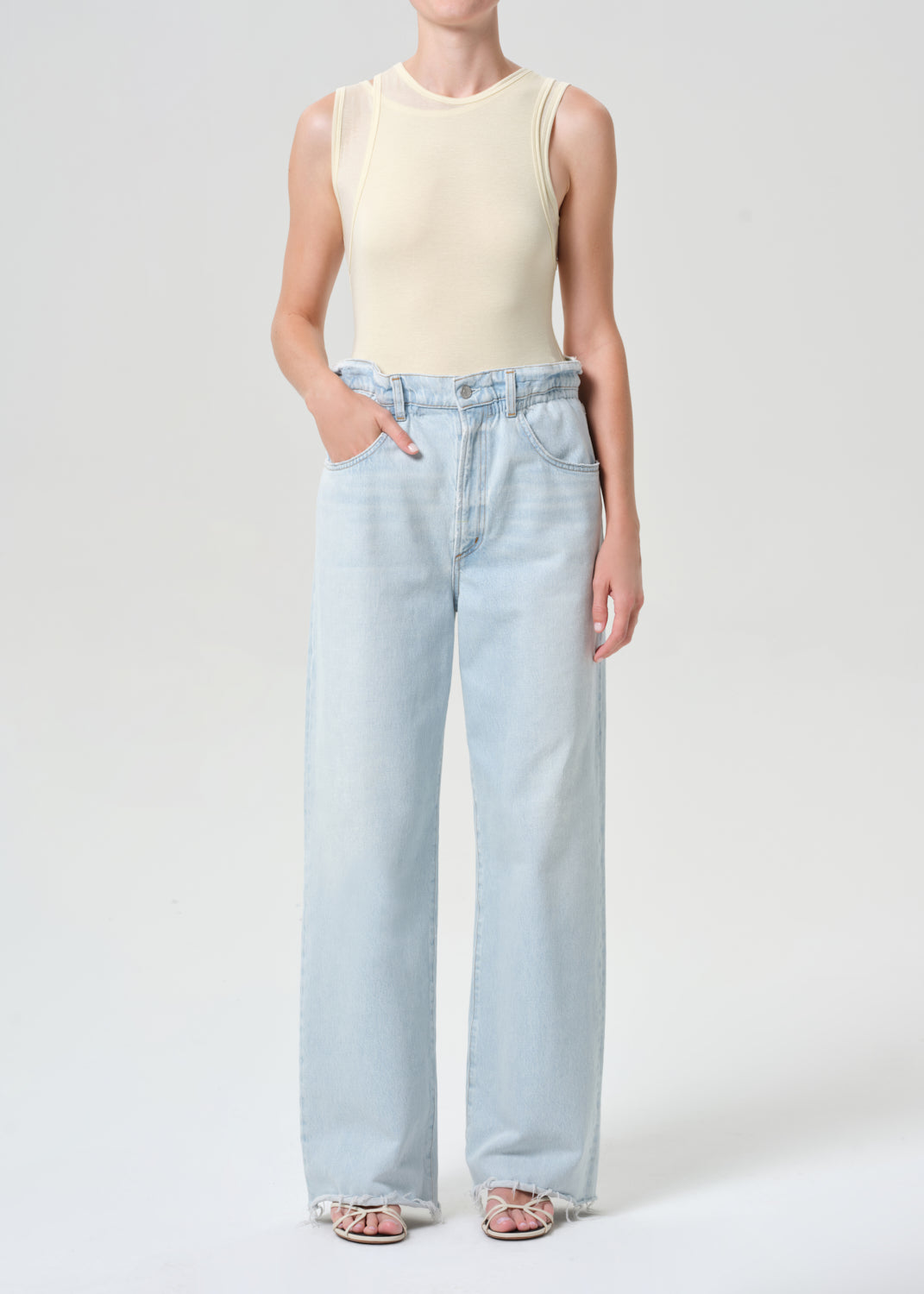 Person wearing a cream sleeveless top and light blue jeans on a white background