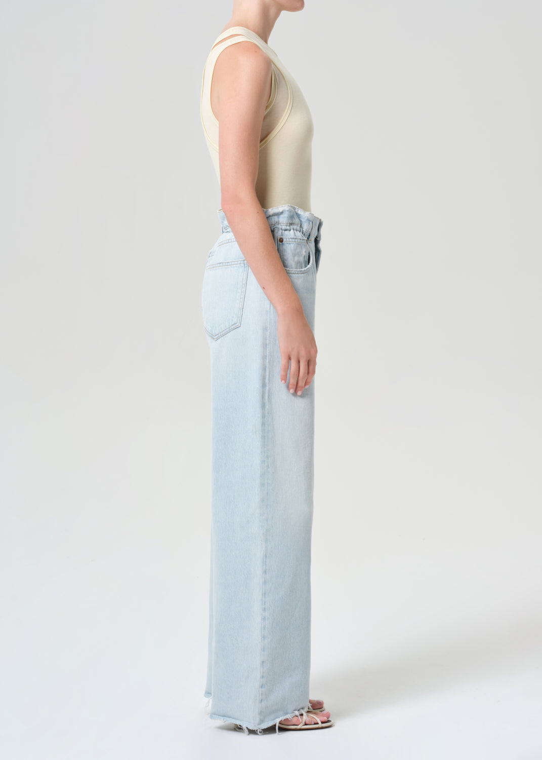 Person wearing light blue jeans and a beige sleeveless top on a white background