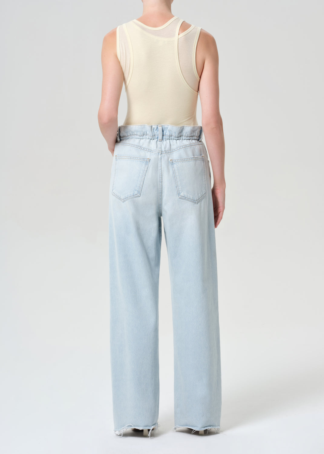Person wearing a cream sleeveless top and light blue jeans on a white background