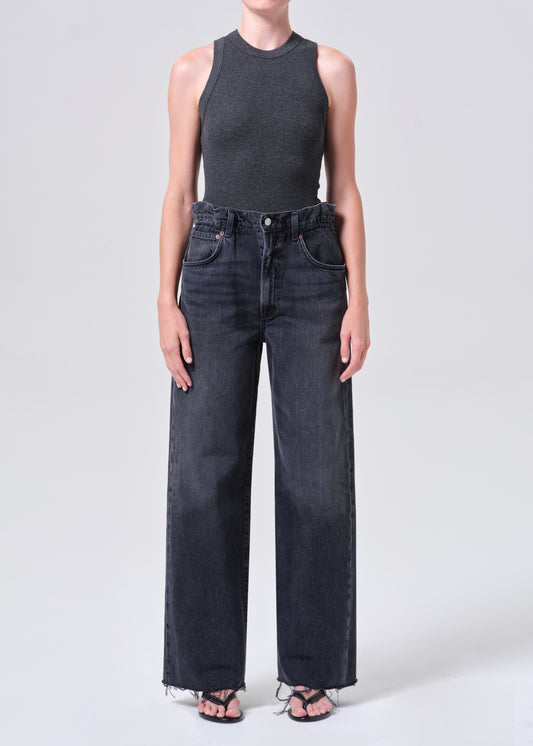 Person wearing a dark gray sleeveless top and black high-waisted jeans on a light gray background