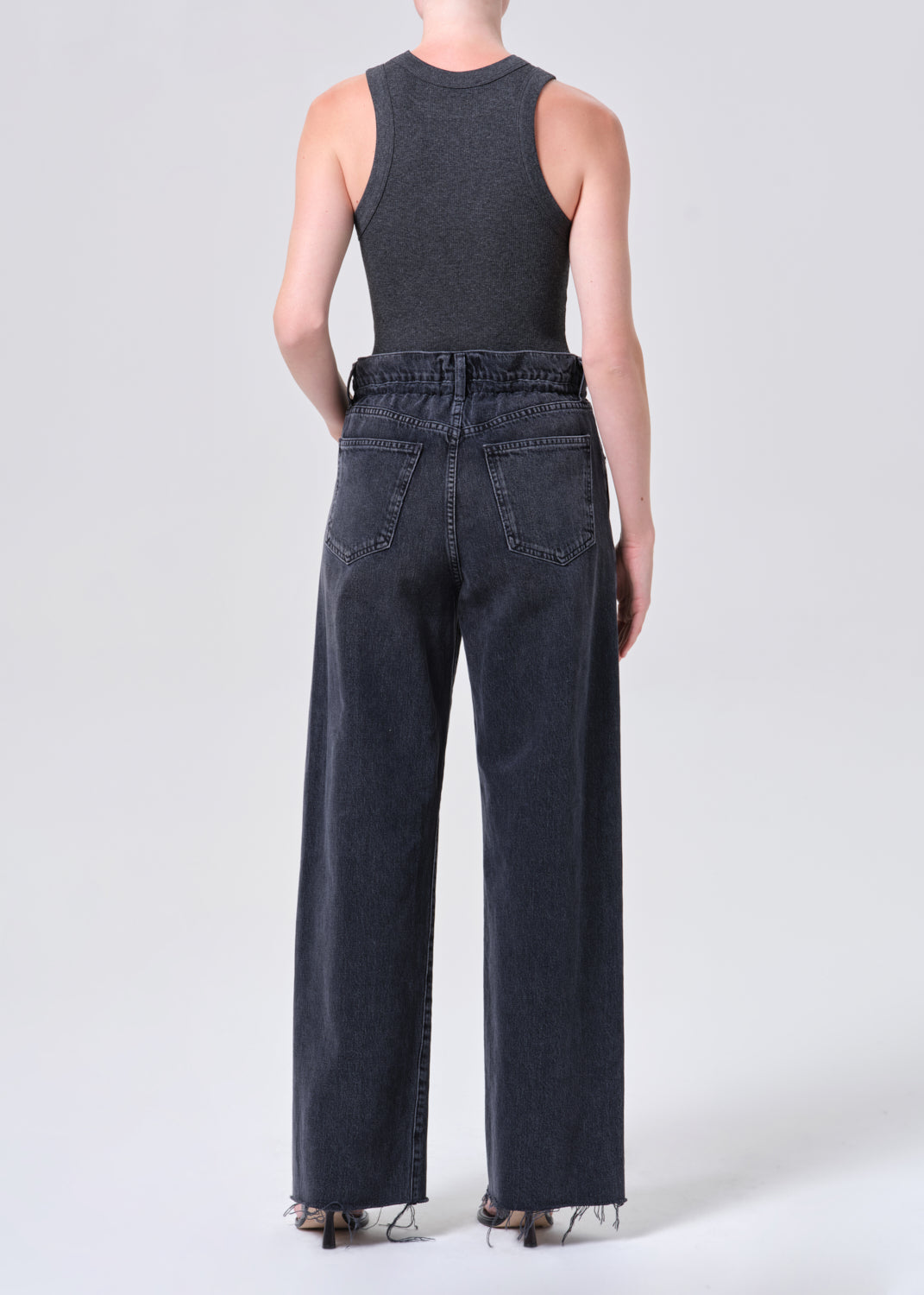 Person wearing a dark sleeveless top and wide-leg jeans on a white background