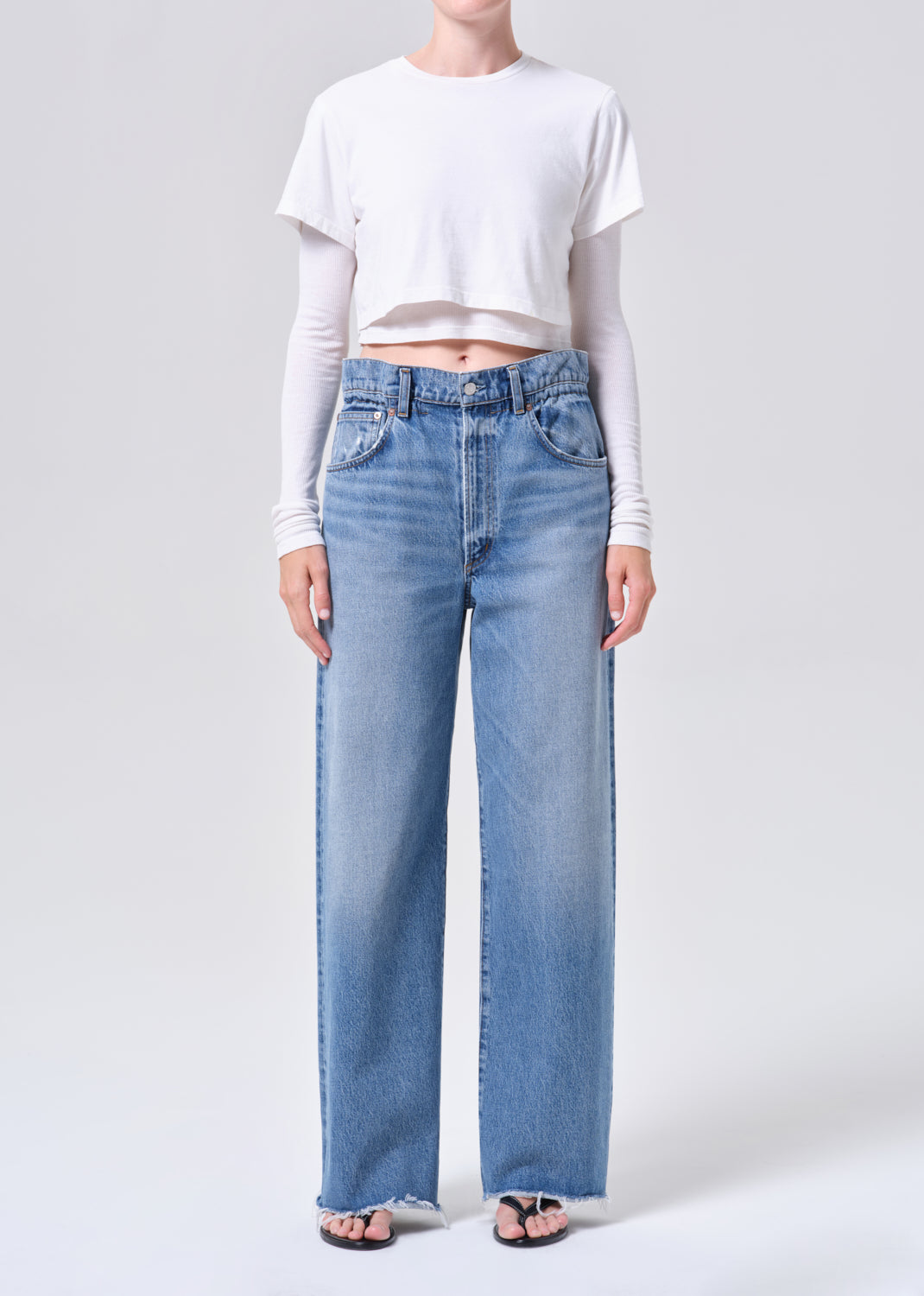 Person wearing light blue jeans and a white cropped top on a plain background