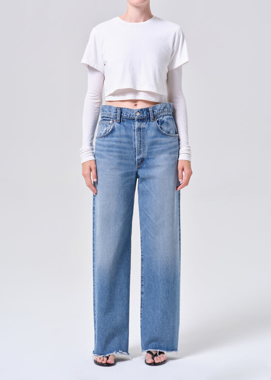 Person wearing light blue jeans and a white cropped top on a plain background