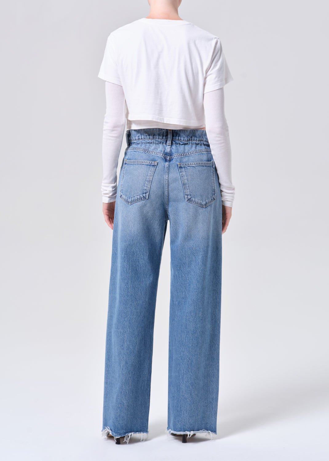 Person wearing light blue jeans and a white top on a plain background