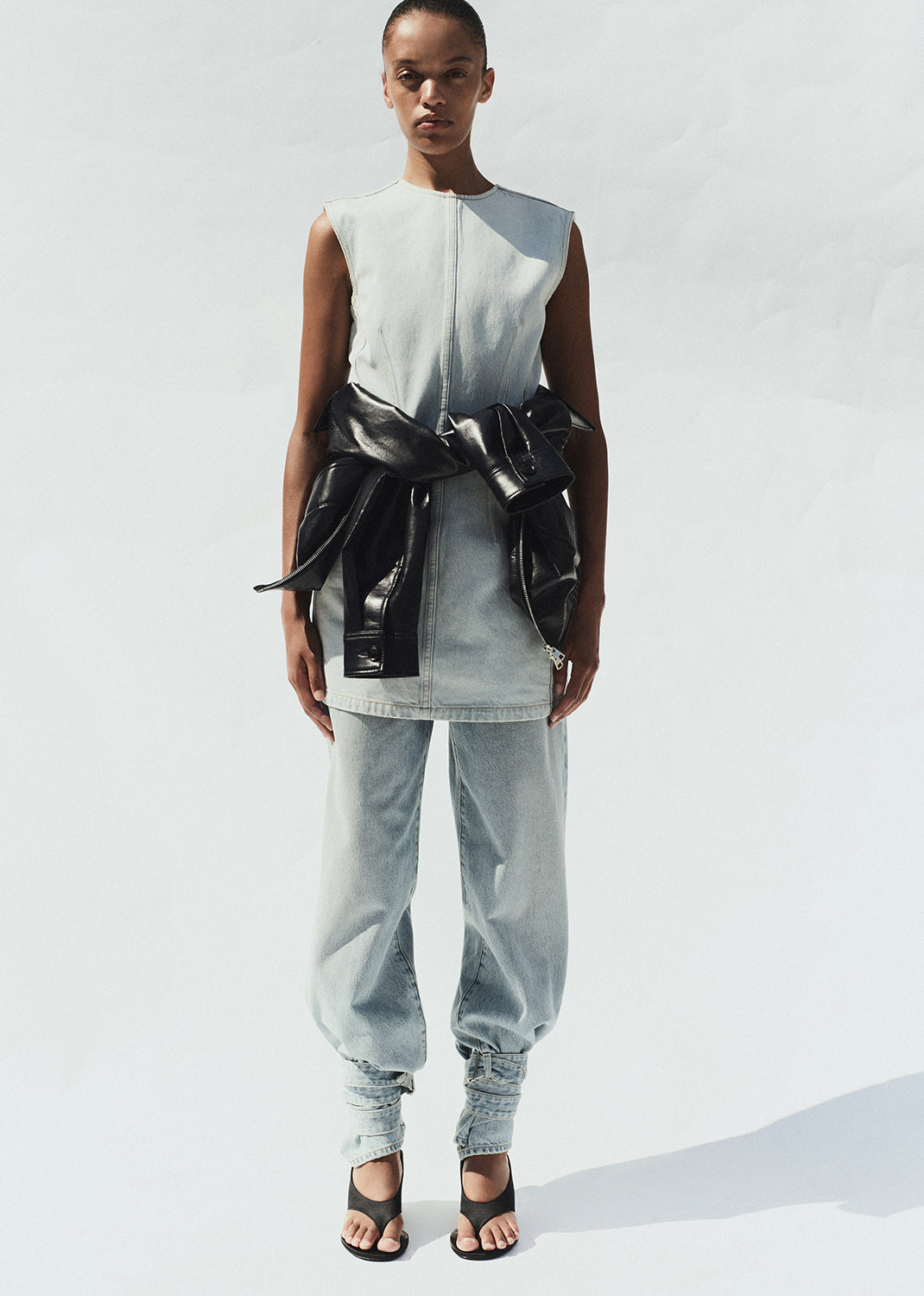 Person wearing a sleeveless top with a black belt and light gray pants on a white background