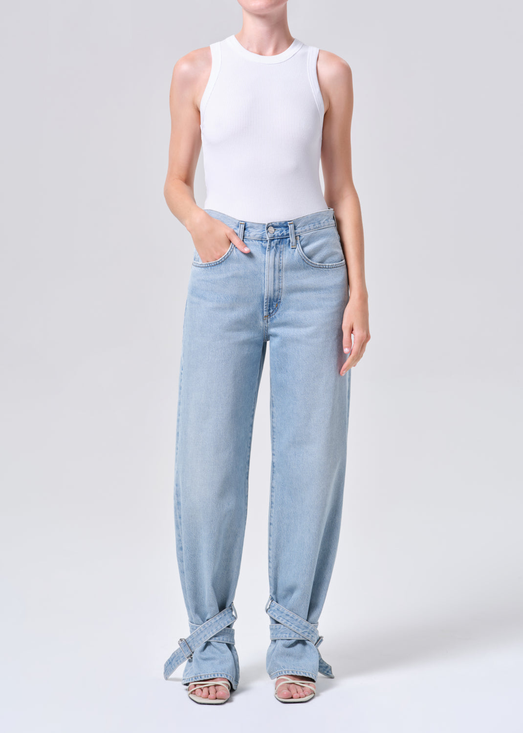 Person wearing light blue jeans and a white top on a plain background