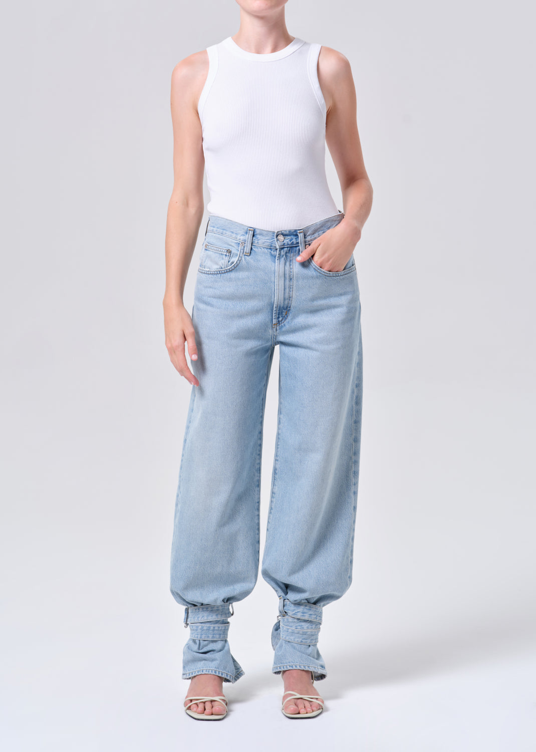 Person wearing light blue jeans and a white sleeveless top on a plain background