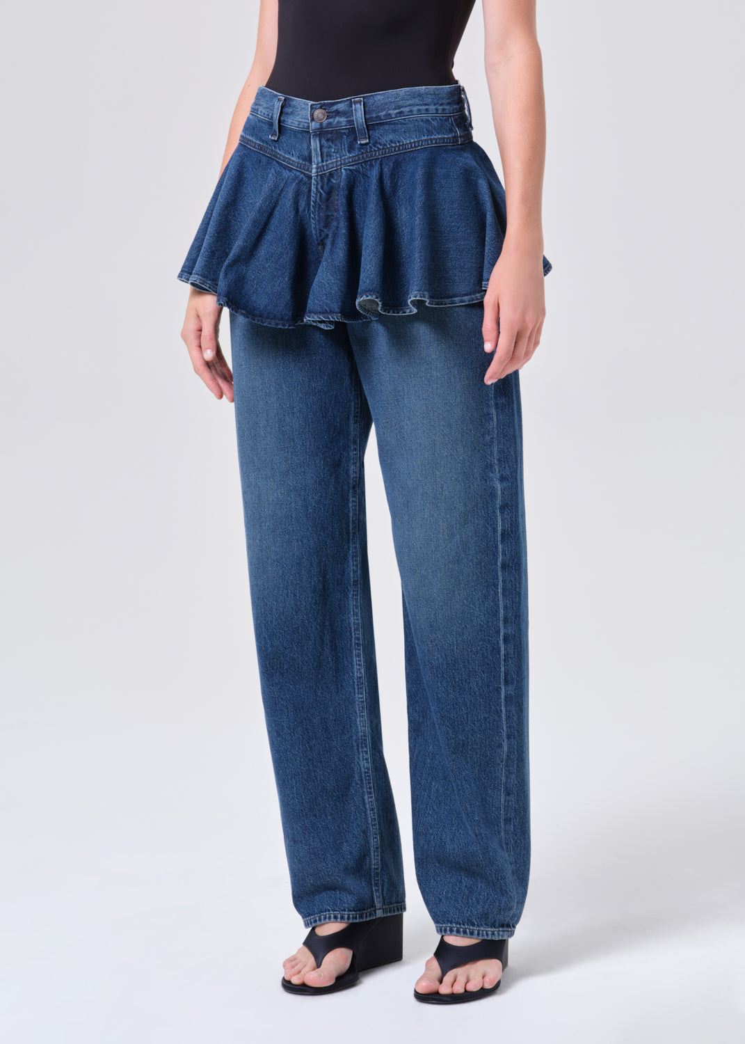 Person wearing a blue denim skirt with peplum waist and high-waisted jeans on a white background