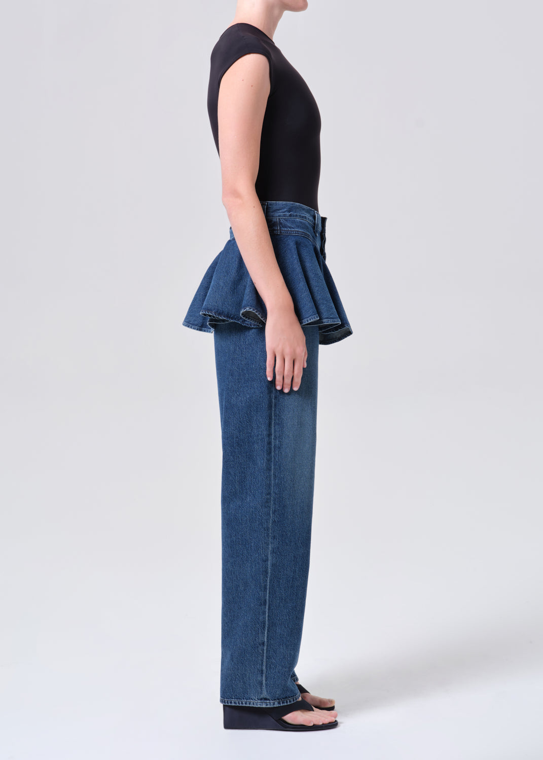 Person wearing a black sleeveless top and blue jeans on a white background