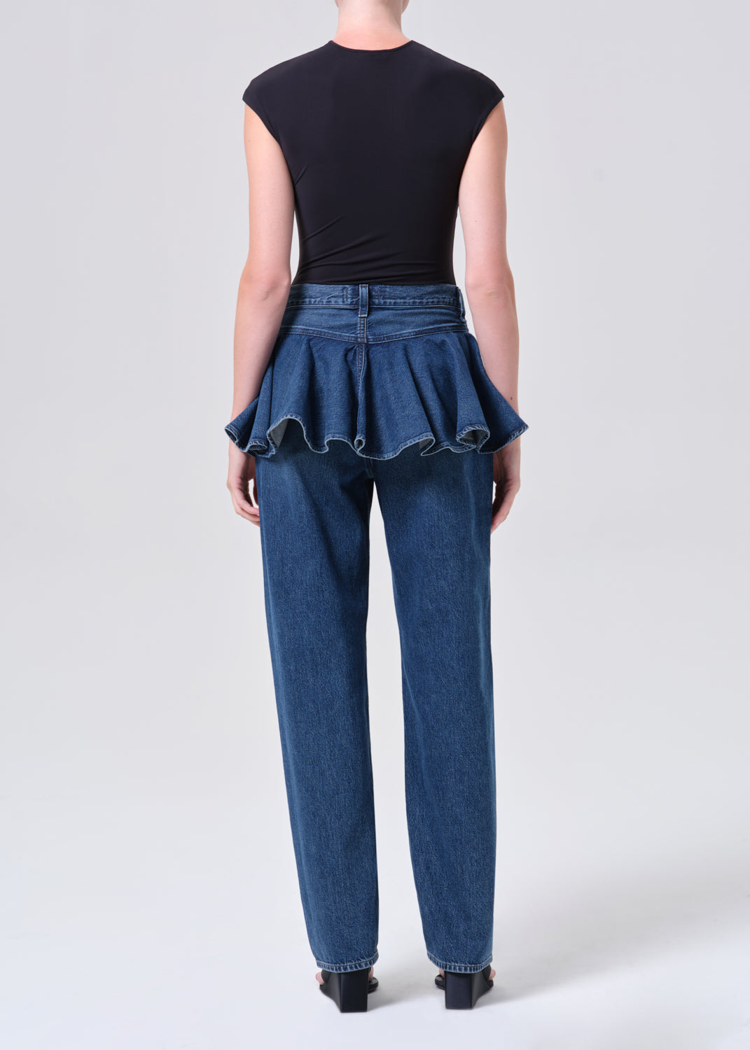 Person wearing a black top and blue jeans with a peplum waist on a white background